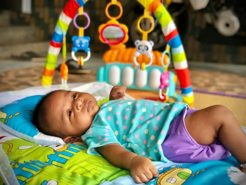 嬰兒遊戲床推薦 baby in pink and white tank top lying on green and blue mat